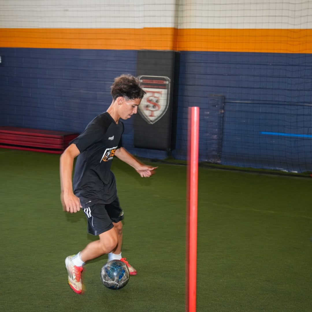 Total Soccer kid playing soccer indoors with a red pole and sports ball on a green field.