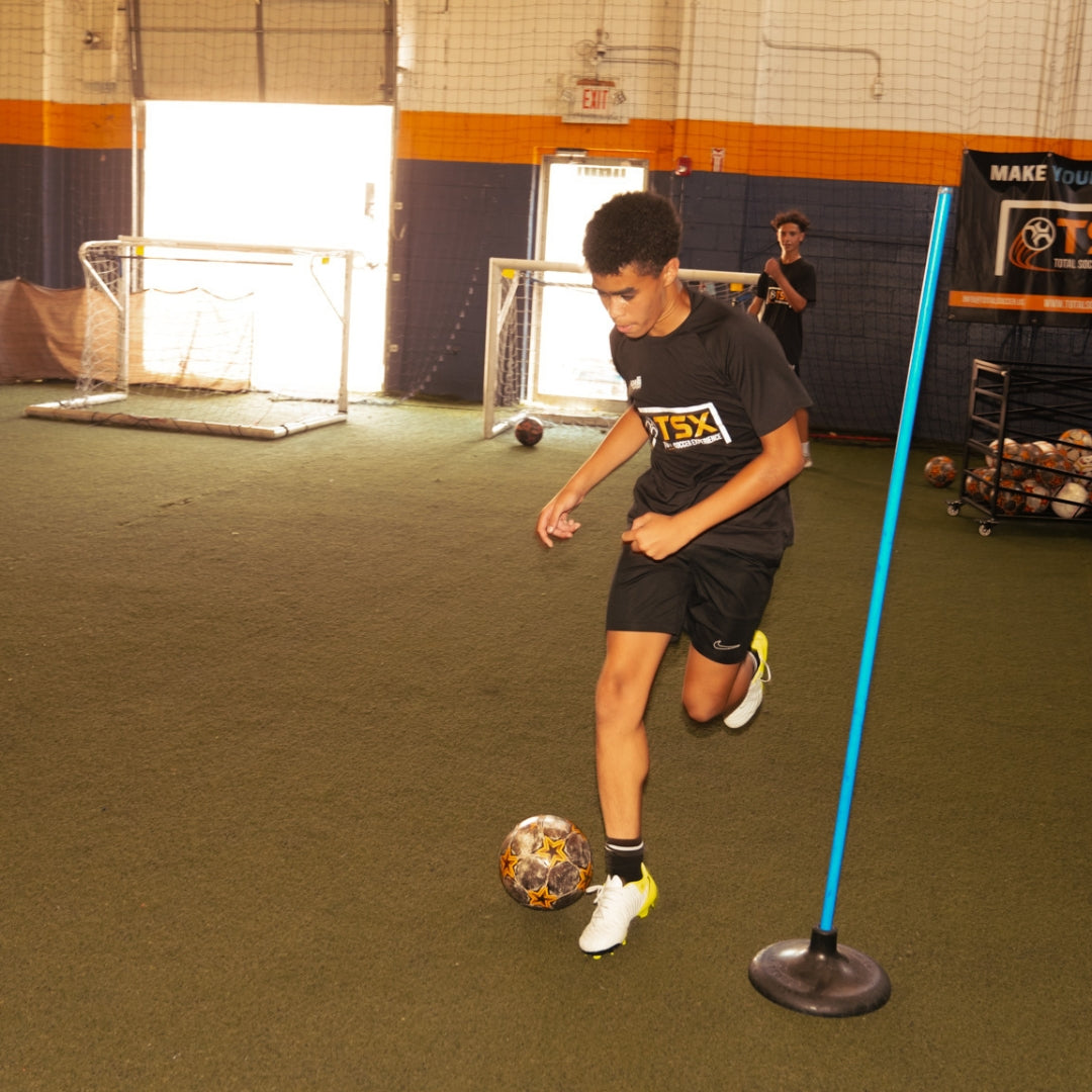 Total Soccer kid practicing soccer drills with a ball and training equipment indoors.