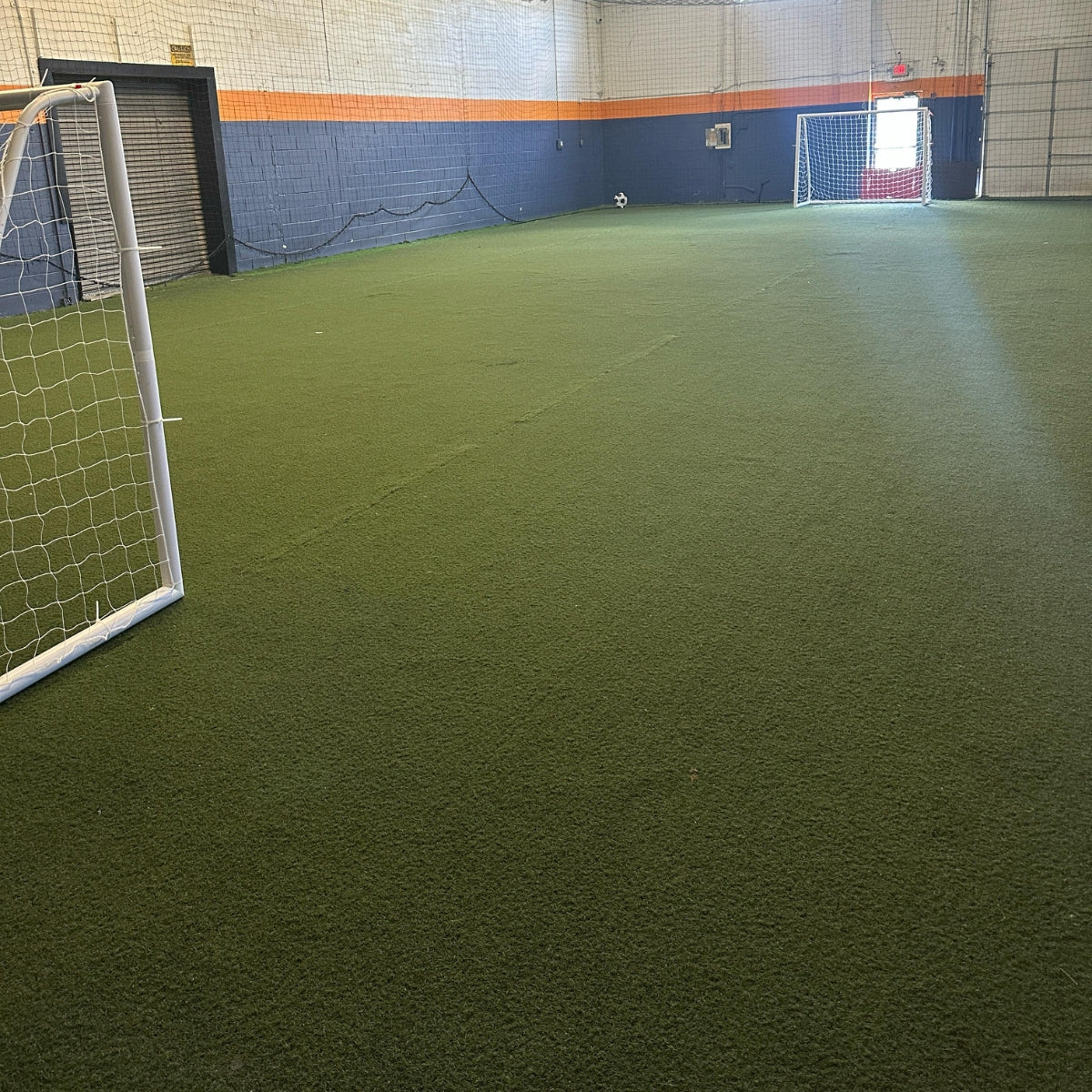 Indoor sports facility with green artificial turf and soccer goals.