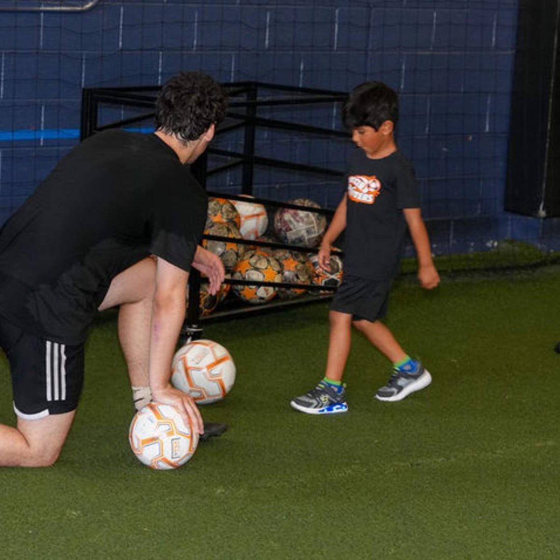 Total Soccer trainer and kid with soccer balls on a green indoor field.