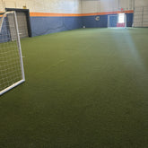 Indoor sports facility with green artificial turf and soccer goals.